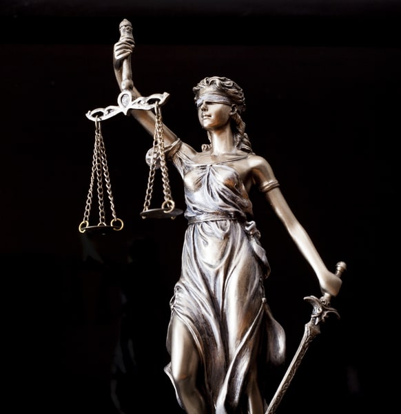 an up close view on a blindfolded statue holding the scales of justice in one hand and a sword in the other.