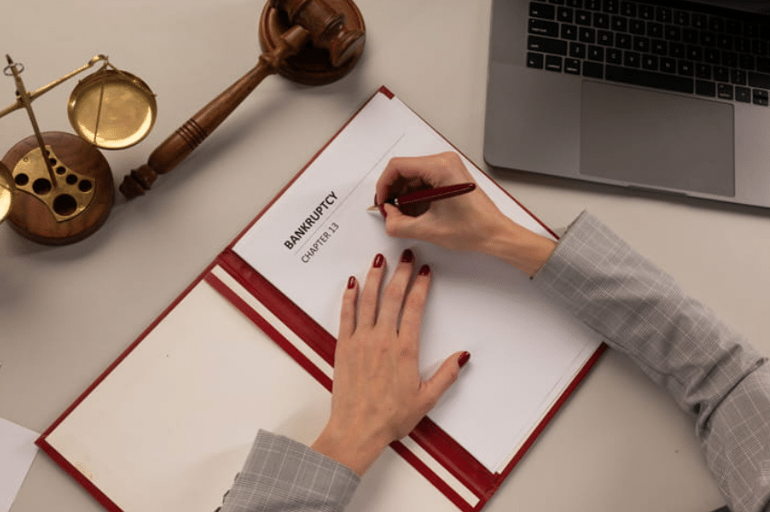 A woman is holding a pen over a document that reads "Bankruptcy Chapter 13."