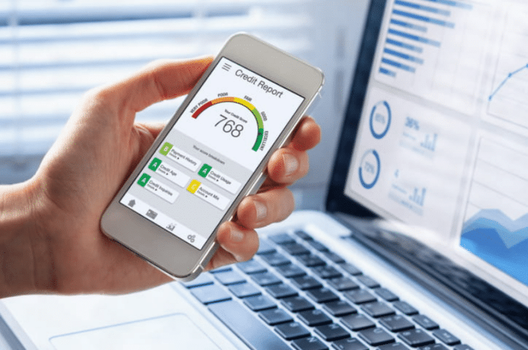 Credit report with Fico Score rating shown on smartphone screen with laptop open in the background