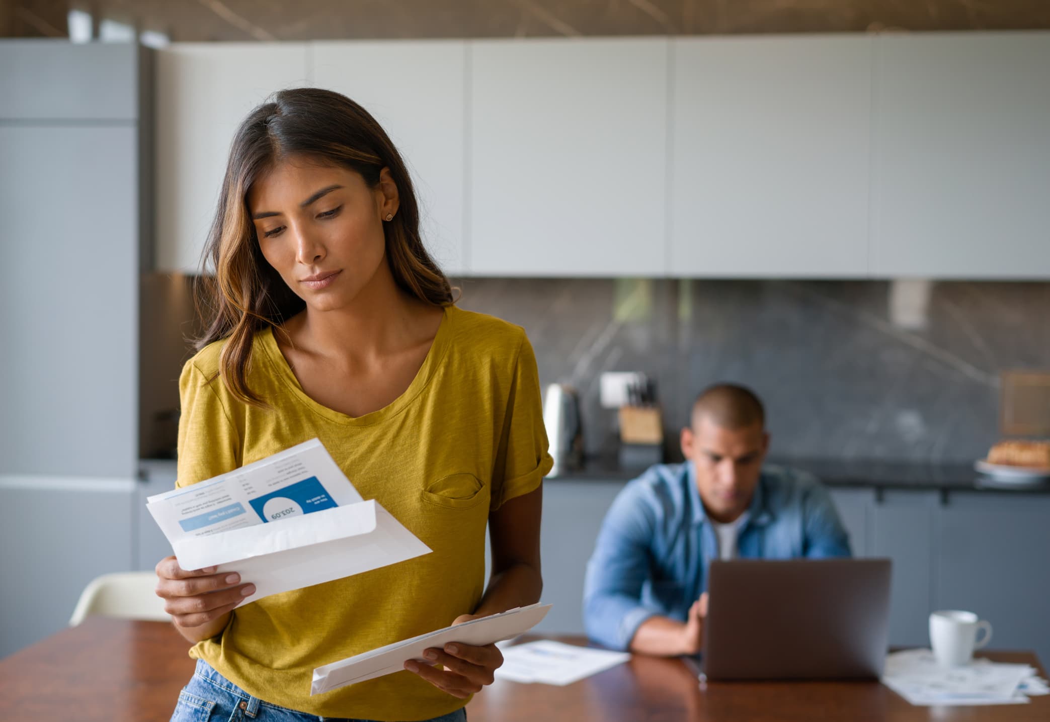 woman looking at debt bill with husband in backround