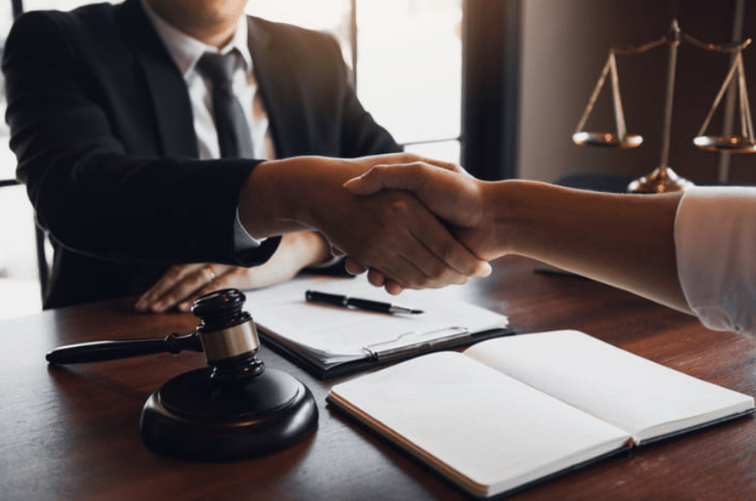 laywer shaking hands with a client with notebook, clipboard, papers, and a gavel between them