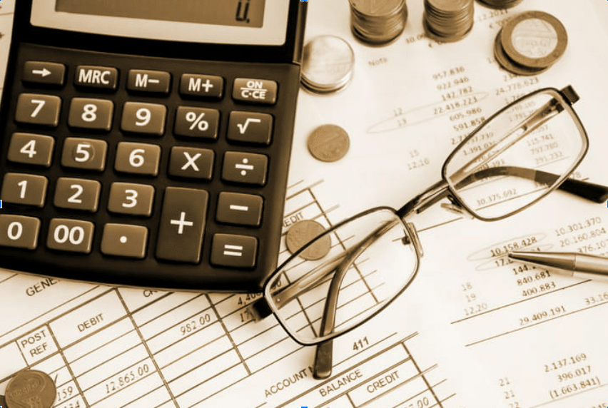 a calculator and glasses layered over budget reports along with coins stacked