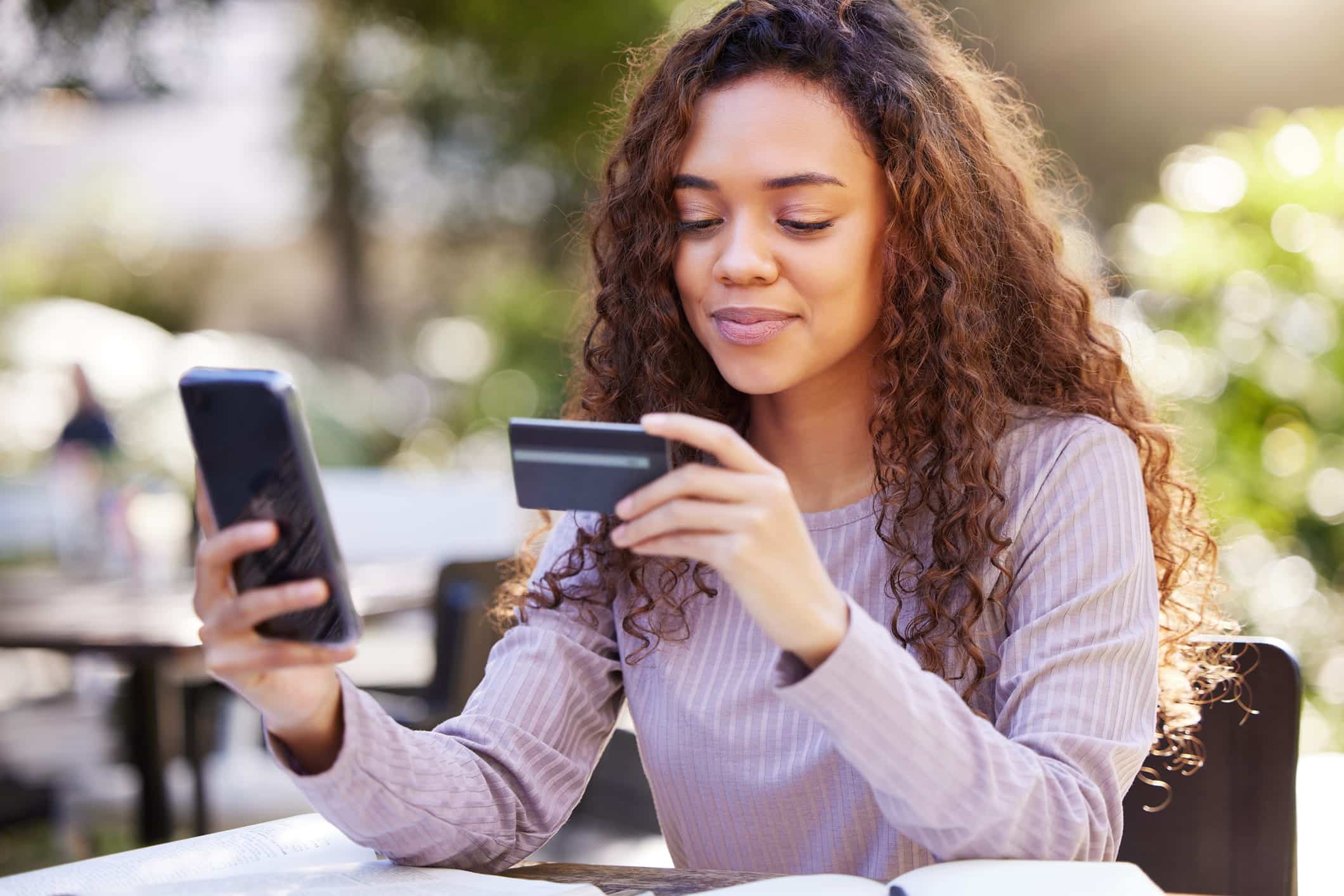 woman looking at her credit card while on her phone