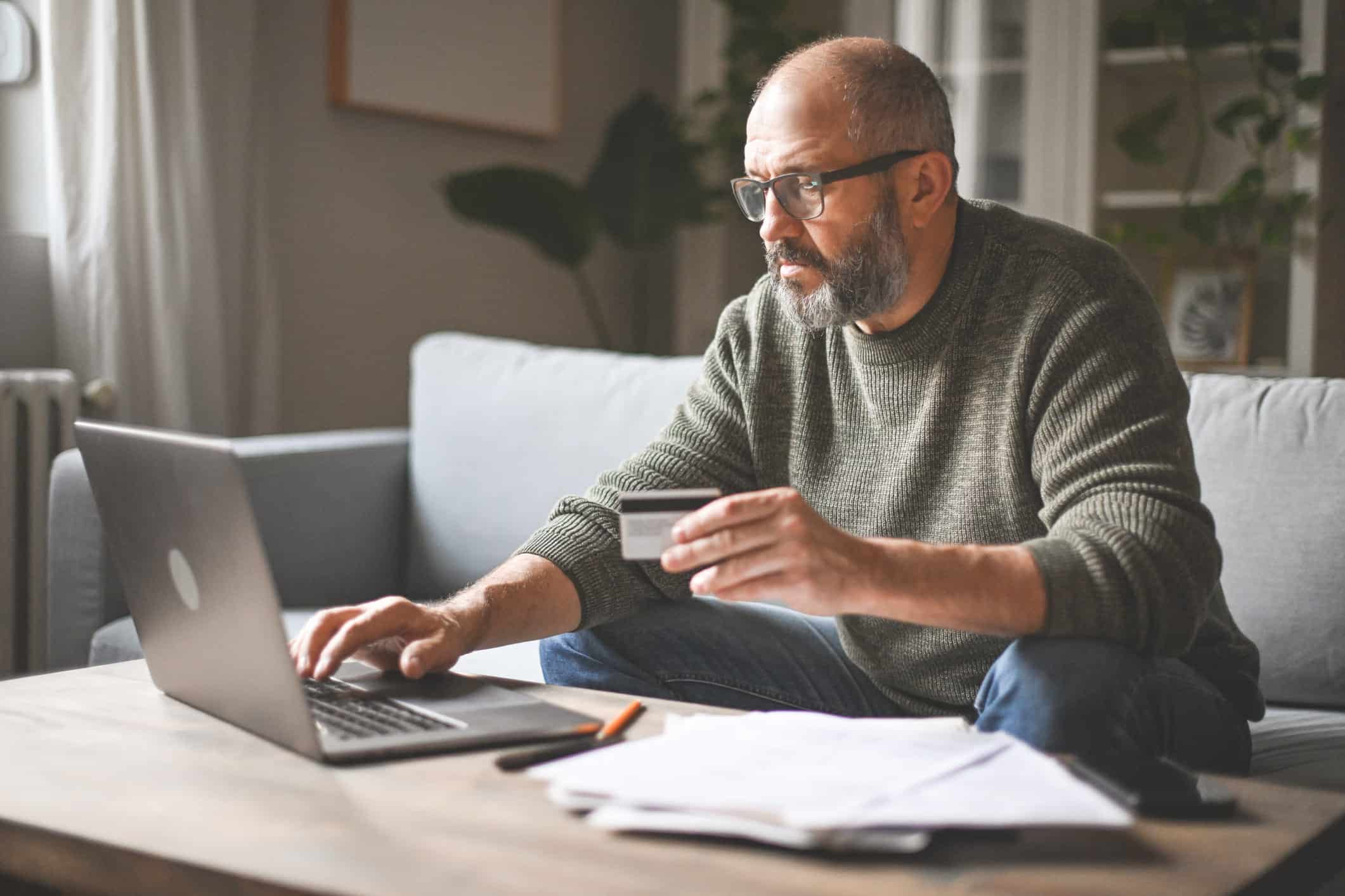 man looking at his laptop screen while holding a credit card