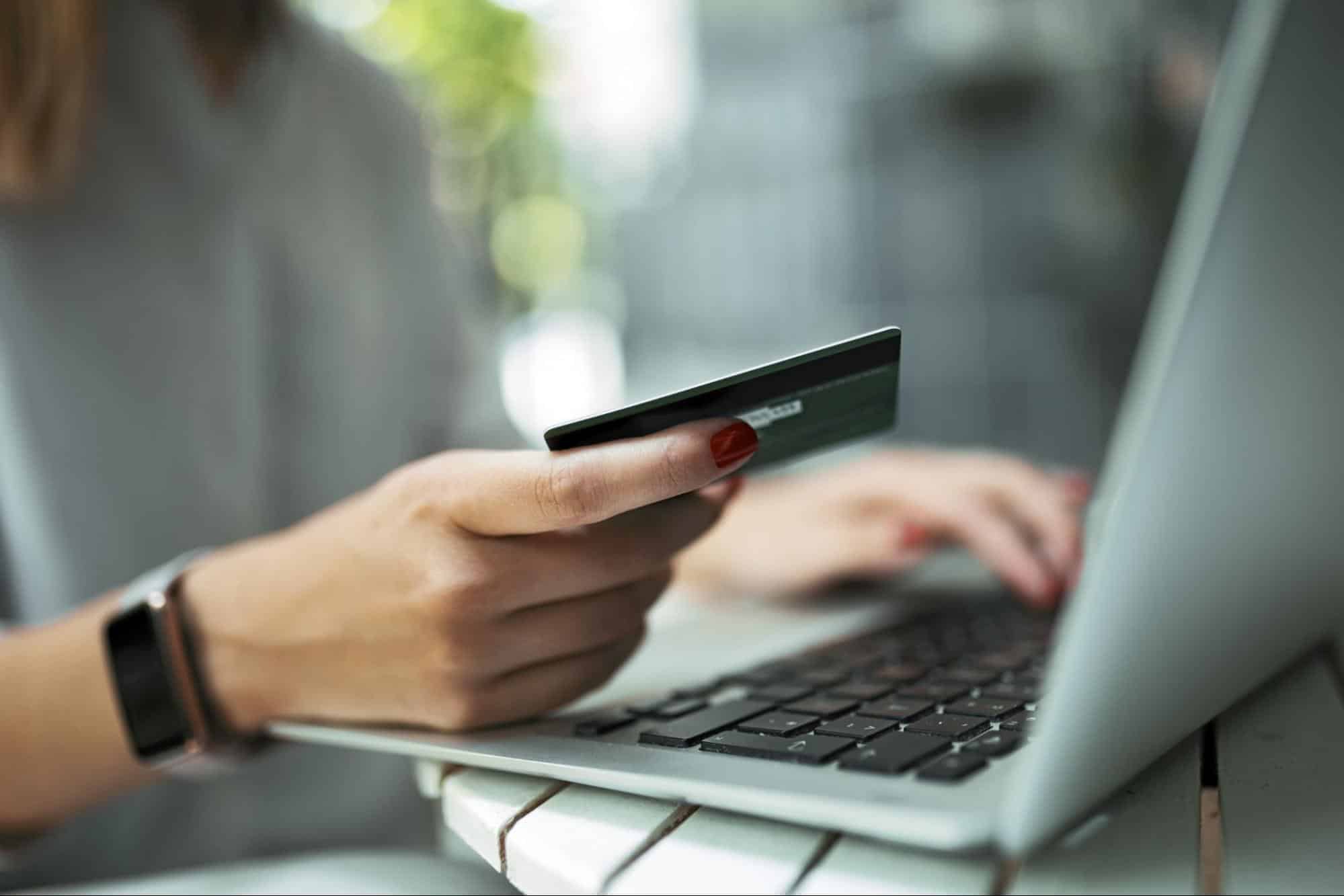 lady typing holding a credit card in one hand and typing on a computer with another